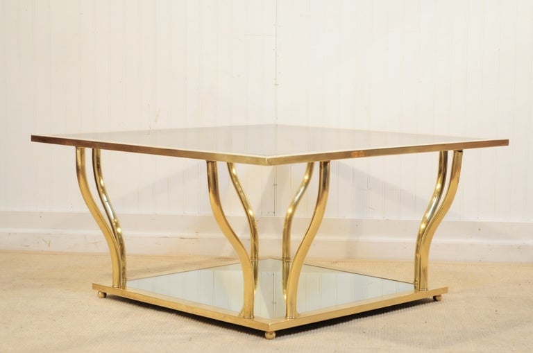 Fabulous vintage, 1960s 2-tier sculptural brass Hollywood Regency Mid-Century Modern coffee/cocktail table. This item features a lightly smoked glass top on the upper tier and mirrored glass on the lower. The form of this piece is stunning and truly