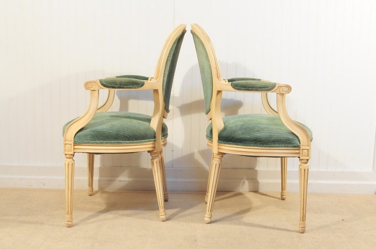 Vintage 1960's Glamorous Louis XVI French Style Paint Decorated Arm Chairs with authentic aged shabby chic distressing to the hand carved frames. Chairs feature padded arms, medallion backs, reeded legs, and antiqued cream distress painted carved
