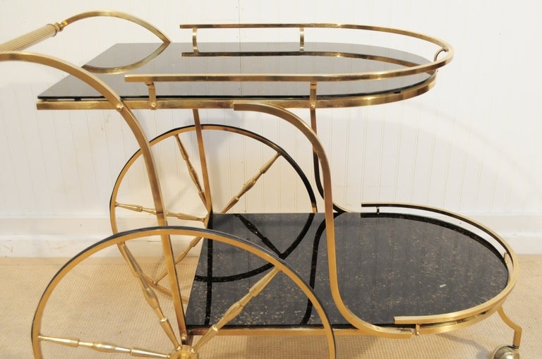 Stunning Vintage Hollywood Regency Brass Tea Cart/Server with 2 tiers of fabulous gold flecks black glass from the early to mid 1900's. This wonderful bar cart features, over sized wheels, reeded handle, 2 glass serving surfaces with brass