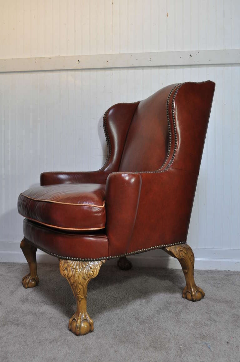 Stately Early to Mid 20th Century High Quality Brown Leather Wing Back Library Chair featuring ball and claw carved feet, double nailhead trim, rolled whimsical arms, and superior comfortable form.