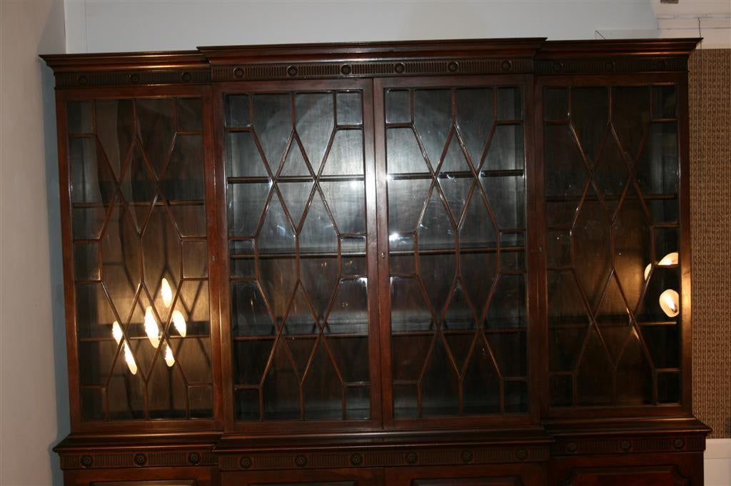 Wonderful Flame Mahogany 2 Part Breakfront from the 1940's by Baker Furniture Co. Item features all individual panes of bubble glass, four doors on top, and four doors on bottom with ample shelving. Carved Medallions adourn the top and bottom of the
