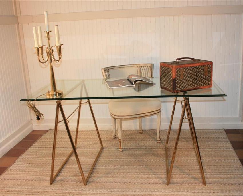 Elegant vintage beveled glass top desk featuring stretcher form brass plated metal sawhorse bases. Very high style item with heavy metal bases and a .5 inch thick beautifully beveled glass top.

Glass Measures: 60