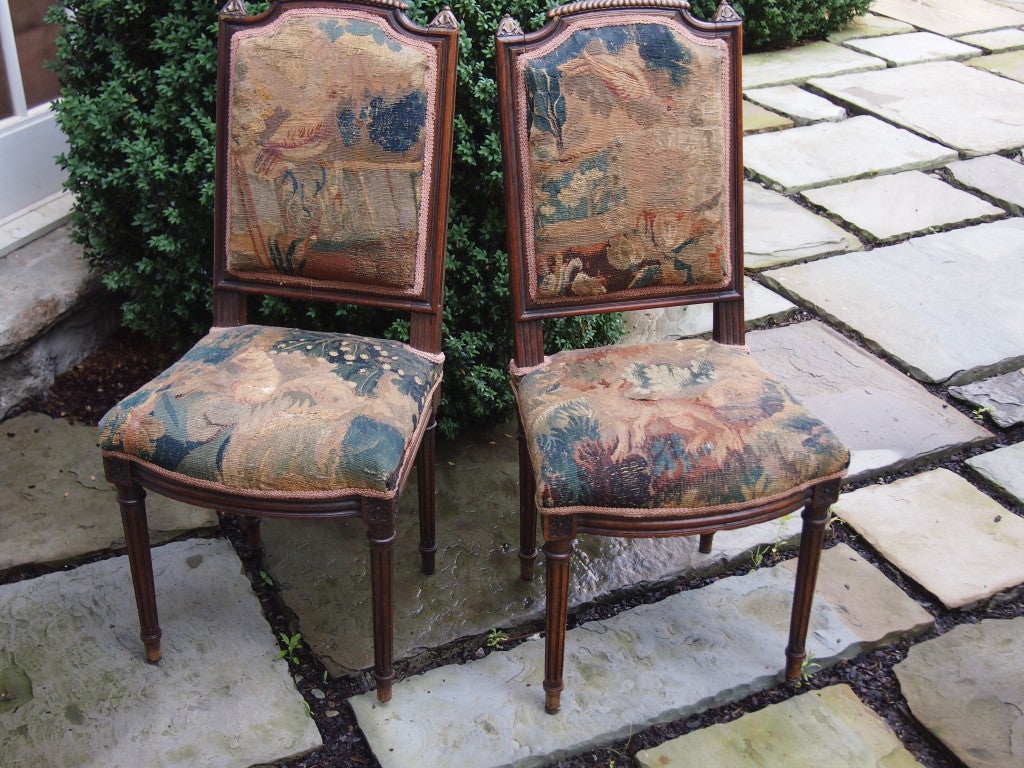 Beautiful and sturdy hand carved French walnut chairs with 18th century verdure tapestry upholstery. Rare addition of birds, squirrels and dogs in tapestry. Damask back panels. Wear commensurate with age.