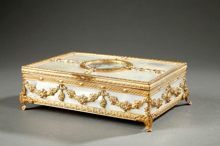 A fine rectangular box in mother-of-pearl and gilt bronze mounts finely chiselled with interlacing, oves and flowers resting on four curved foliated feet. Friezes with gilt bronze garlands decorate the four faces of the box. A small circular