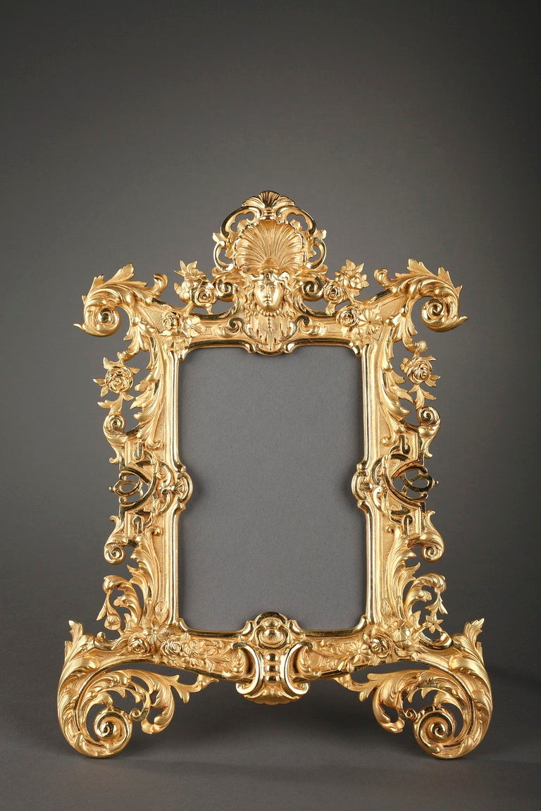 A gilt bronze frame richly sculpted with garlands of flowers, roses and scrolling foliate terminating with scrolling foliage. Openwork interlacings on both sides and a mascaron crowned with a shell atop complete this beautiful set highly