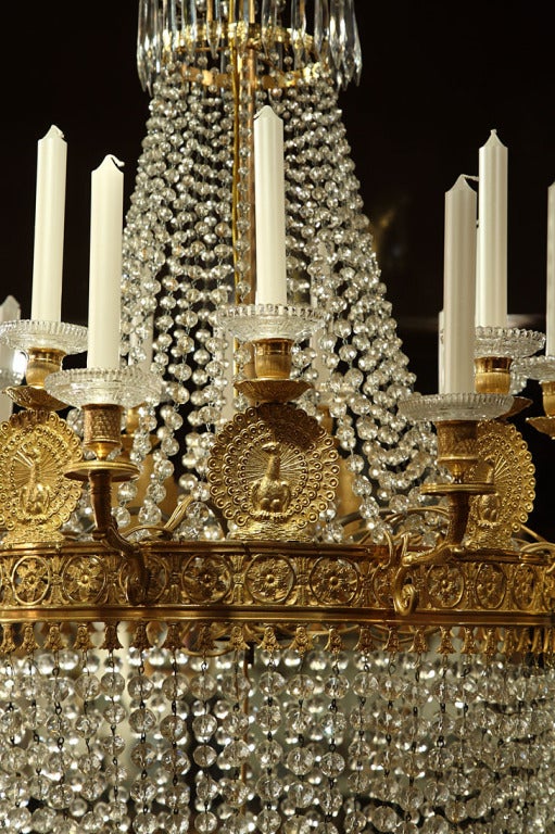 A crystal chandelier with eighteen gilt and chiseled bronze light branches, nine of them are hanging from a circular floral decorated crown, alternating with nine other lights shaped as very special peacocks with eagle heads. On the top part of the