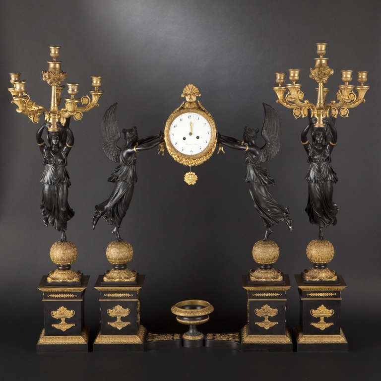 Large bronze three-piece clock garniture, Empire Style

Large gilt bronze and patinated bronze three-piece clock garniture. Clock held by two Victories atop spheres with palmettes and two rectangular plinths held by an urn cross-bar. Pair of