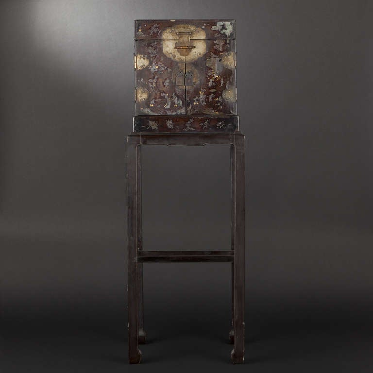 Lacquered wood cabinet. China, 17th century.  Black-lacquered wood cabinet with inlaid mother of pearl decoration of pagodas, pine trees, figures and phoenix.  Fitted with two doors and fall-front reveals three interior drawers.  Support added
