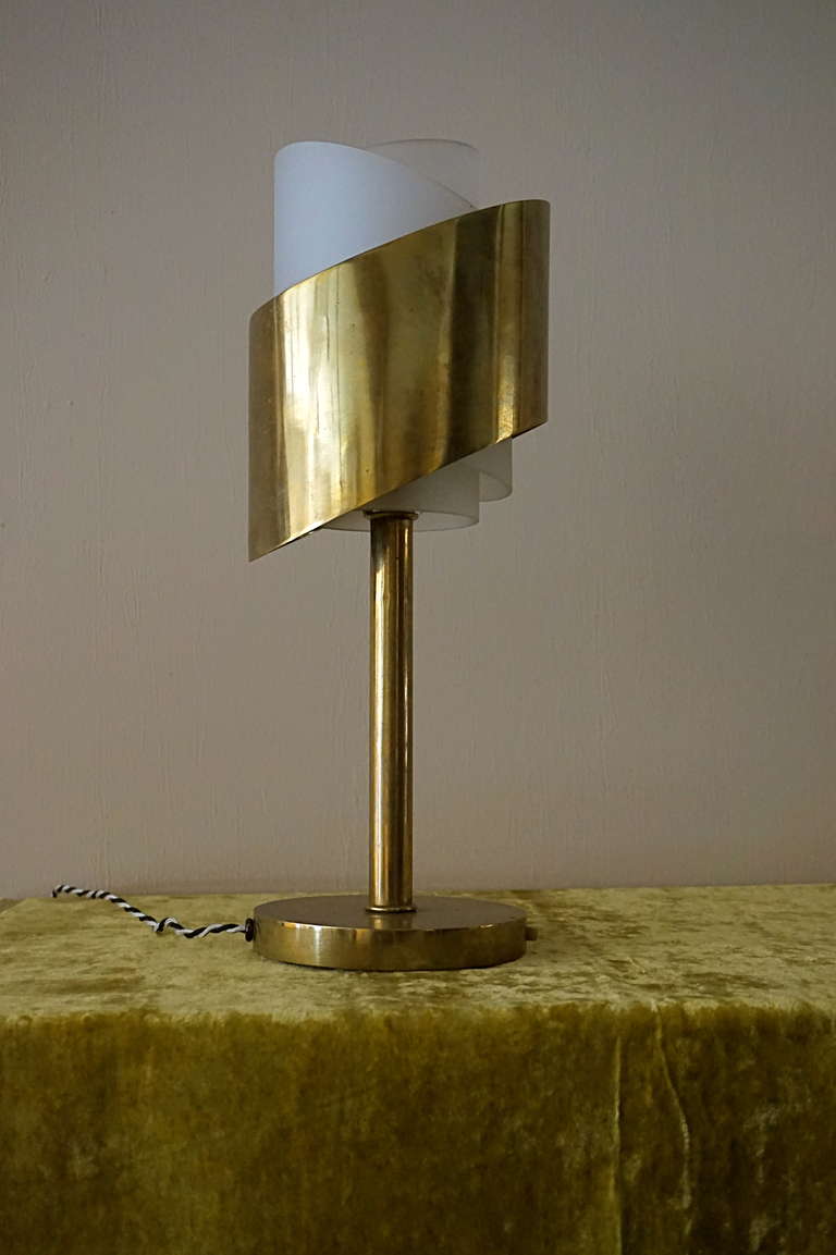 Table lamp, circa 1928
Polished brass, lampshade spirally-cut, enclosing two concentric satin glass cylinders, resting on a tubular stand with circular base, decorated with two switches on the perimeter

Signed with the designer's mark 'J.