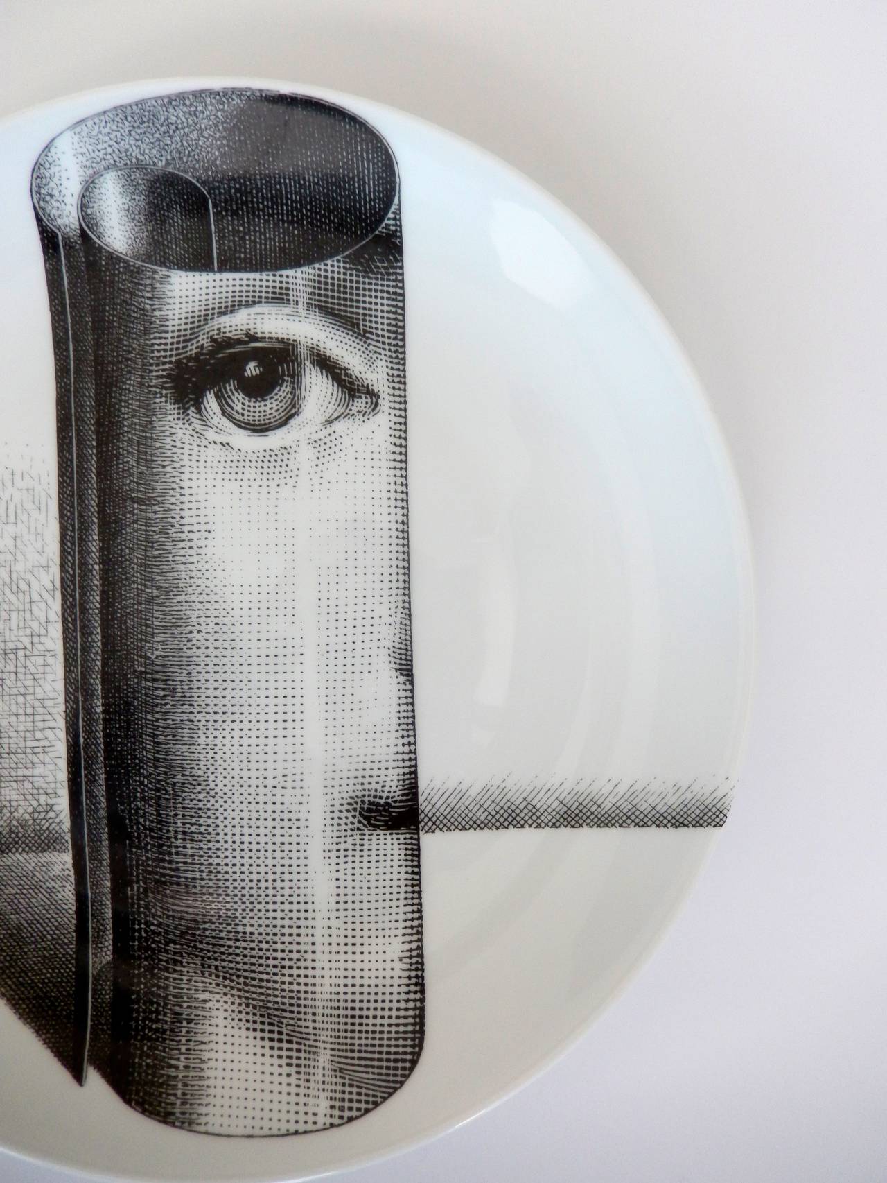 An early production plate by Fornasetti with a striking, surreal image of the eye of his muse, Lina Cavalieri, staring back at the viewer. The cylindrical form resembles a scrolled piece of paper. Very intricate and fine graphic design.

A similar