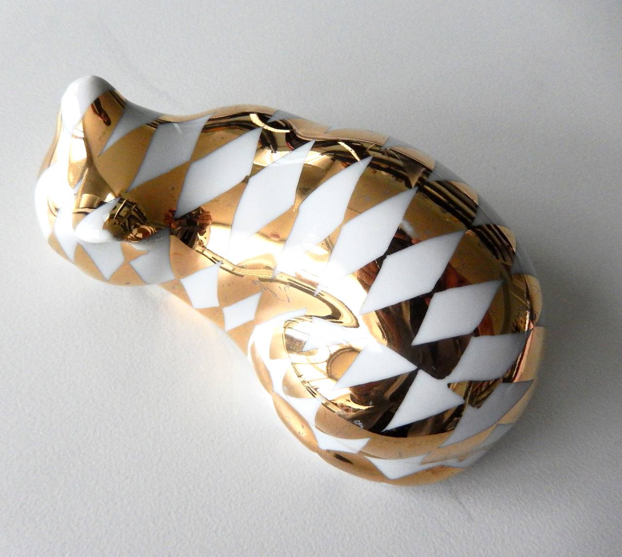 A sleeping ceramic cat figurine with a luxurious gold lustre harlequin pattern by Piero Fornasetti. Marked.