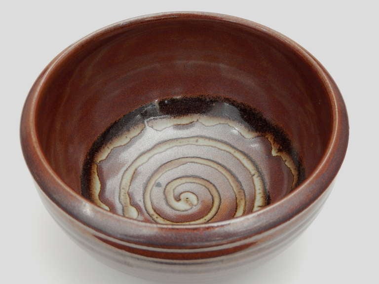 A beautiful small bowl by the American potter Val Cushing 
(b. 1931).   Cushing creates utilitarian vessels reflecting his interest in function. This bowl, inspired by natural forms has a rich brown glaze and an interior spiral design.  Cushing's