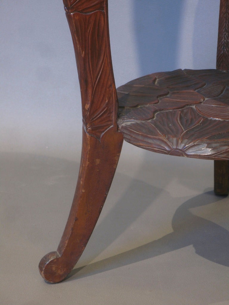 Two tier circular tripod table, extensively carved with large, exotic looking flowers.