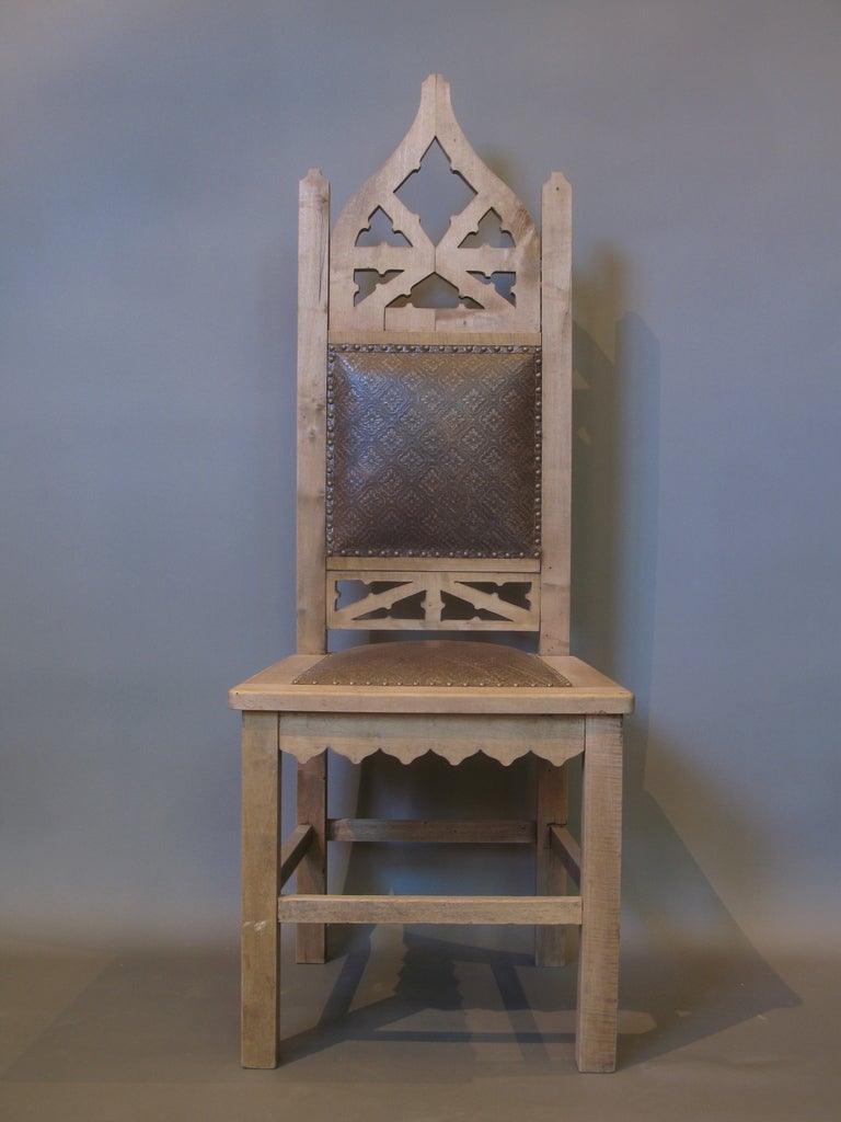 Pair of neo-gothic chairs with high backs and gothic fretwork and carved details. Upholstered in embossed leather.
