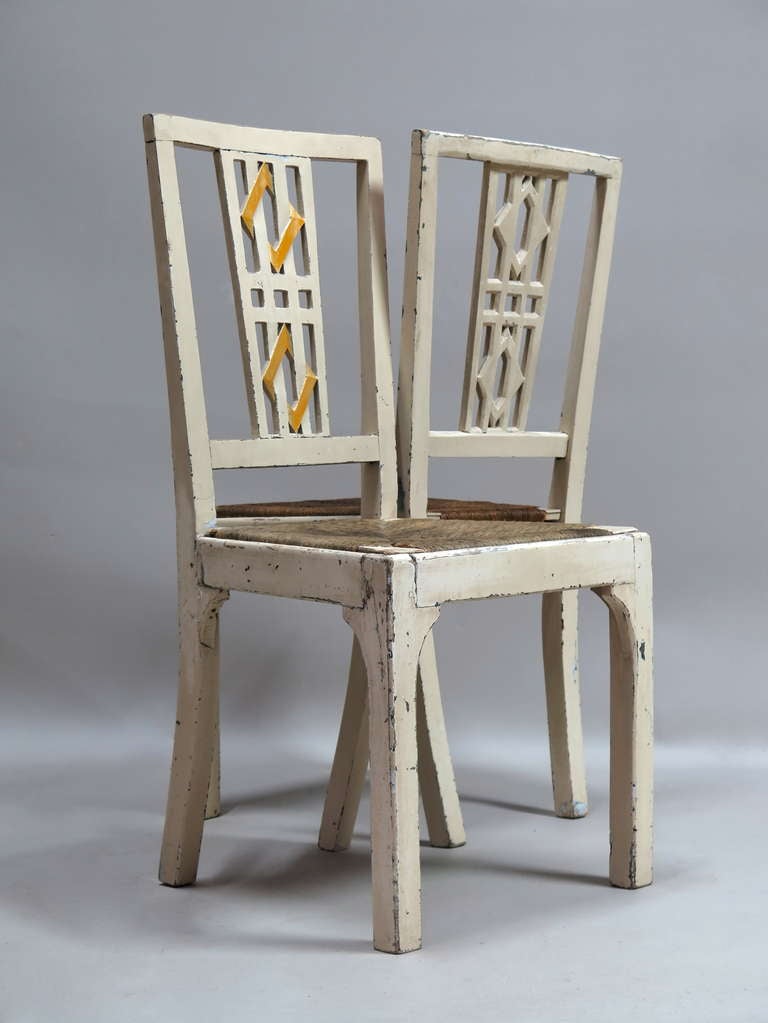 Very rare pair of side chairs of charming design. Large trapezoidal rush seats, square legs and backs adorned with a pair of losanges interlocking with vertical rods. The losanges are painted in two tones of yellow against the overall off-white