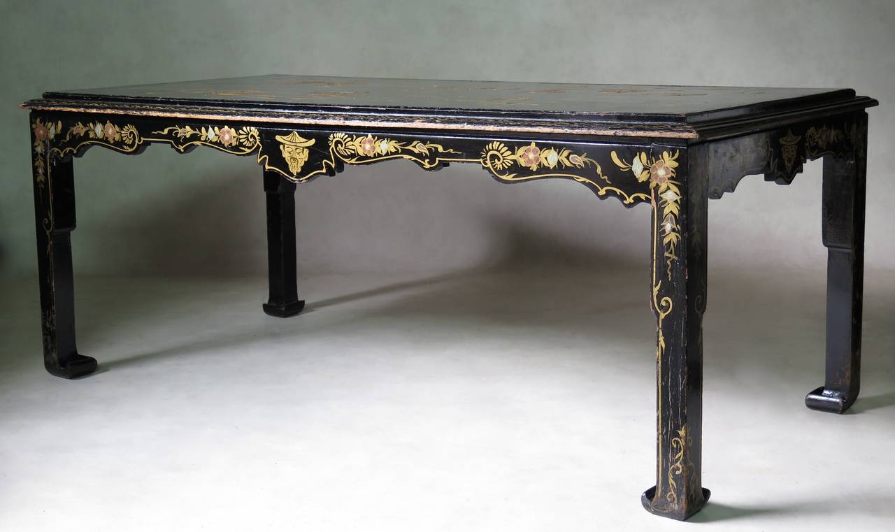 Großer Ess- oder Mitteltisch aus schwarz lackiertem Holz mit goldfarbenen Verzierungen an der Schürze und den Beinen. Aufwendig verzierte Tischplatte mit leichtem Relief.
Eine dicke Glasplatte schützt die Tischplatte (nicht abgebildet).