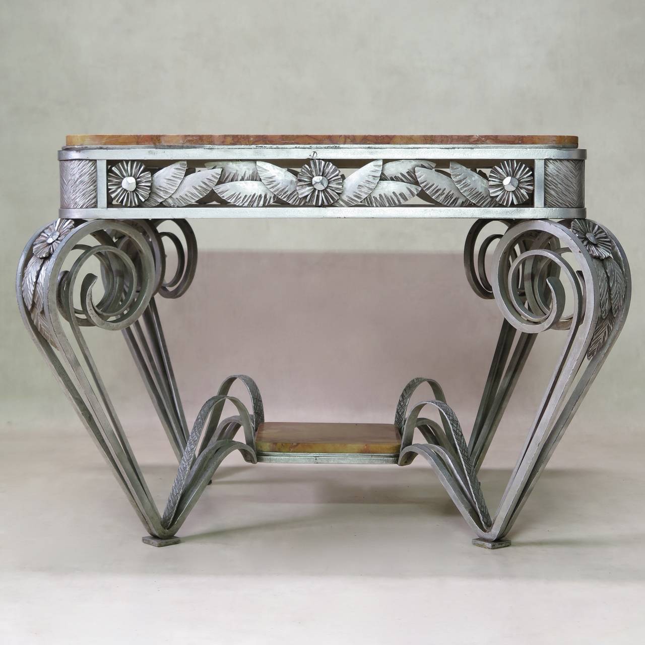 Beautifully crafted, hand-forged iron centre table with two tiers of red marble. The apron and knees are decorated with large, stylized daisies. Exaggeratedly swirled details, dramatically tapering base. Original silver finish. Unique and stunning