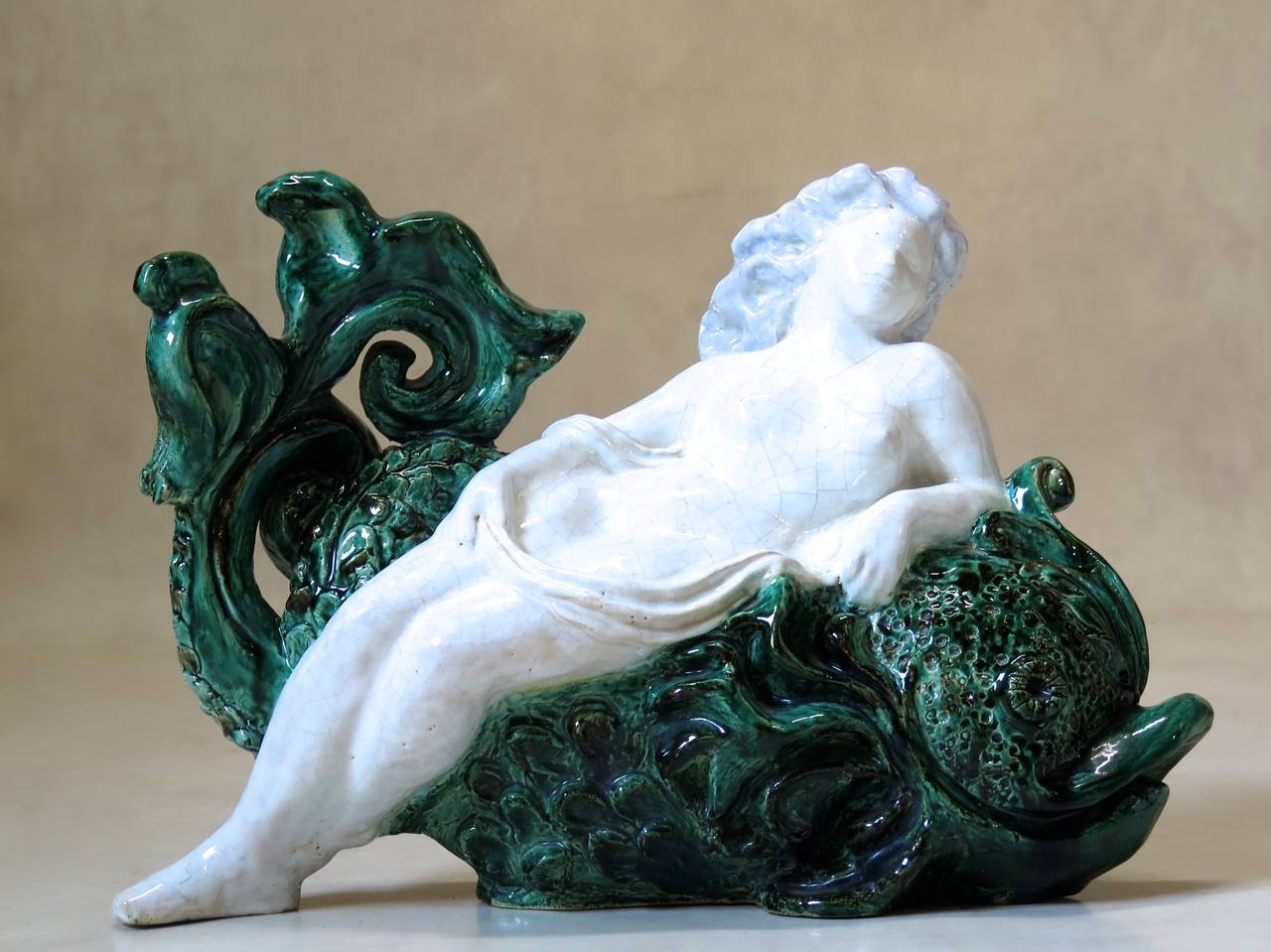 Lovely glazed ceramic representation of a nude woman reclining on a dolphin's back. Craquelure finish on the woman. Signed and dated 