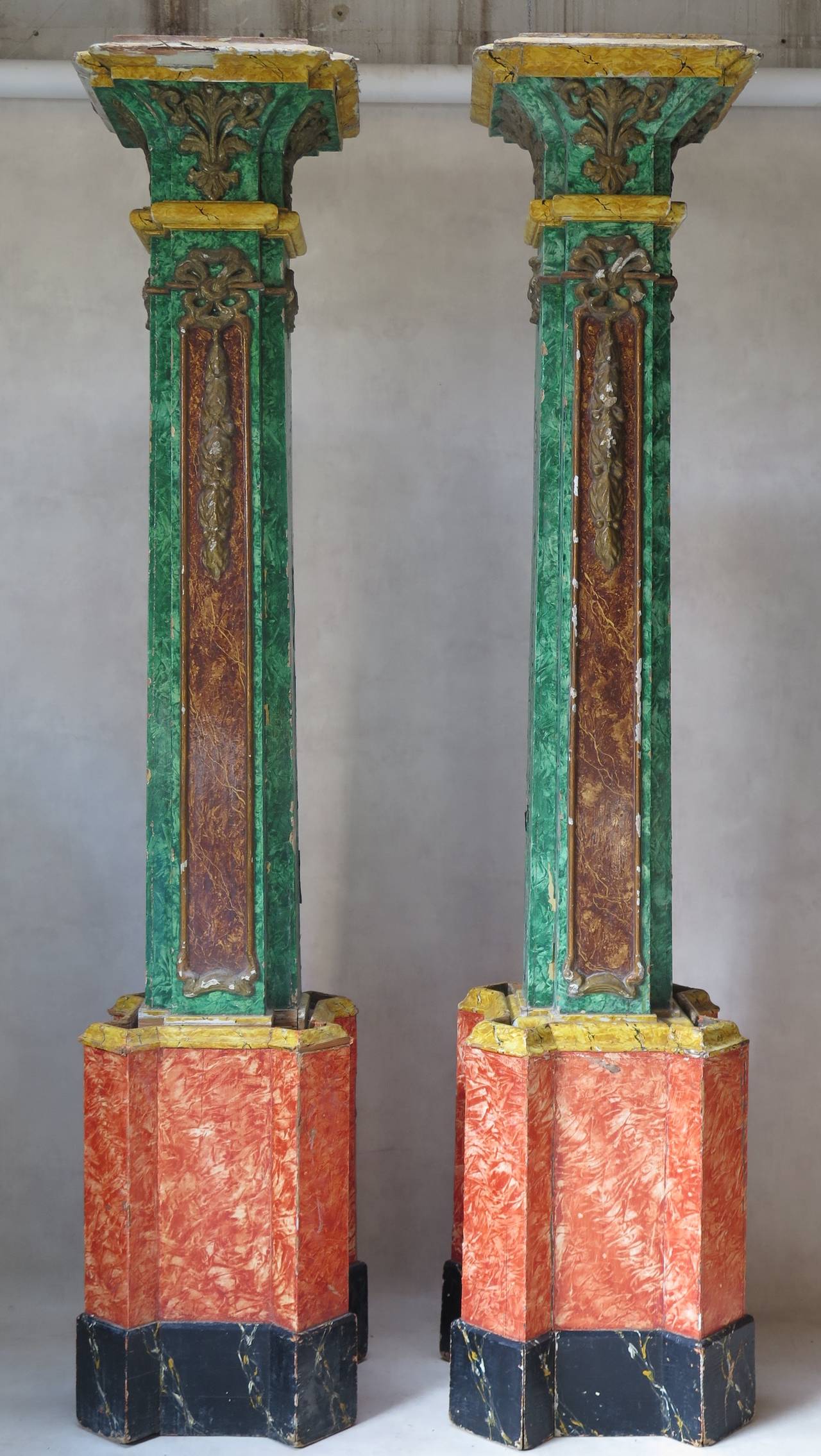 A very tall pair of decorative wood columns in two parts (bases and tops), painted in polychrome marble trompe l'oeil. The moldings on the tops parts (painted in antique gold) are in papier mâché.
