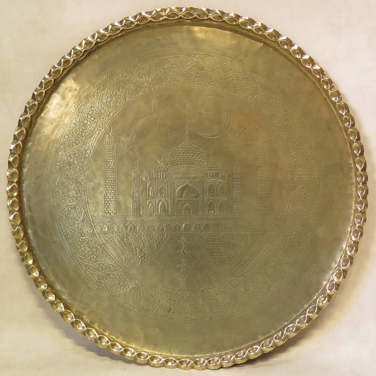 Very large brass tray, hand-hammered and chiselled, with a floral frieze surrounding a central medallion representing the Taj Mahal beneath a starry and moonlit sky. Pie-crust edge.

Could be used either as a coffee table top, or as a wall