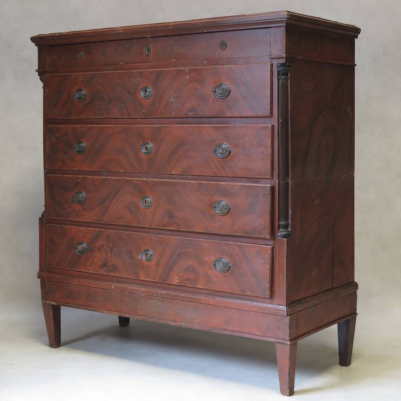 Tall French Empire-style commode. The pine wood is painted in a faux-bois trompe l'oeil imitating mahogany. Wood columns on either side are painted a darker color. 
The chest is in two parts (top and bottom). The divide can be seen from the side