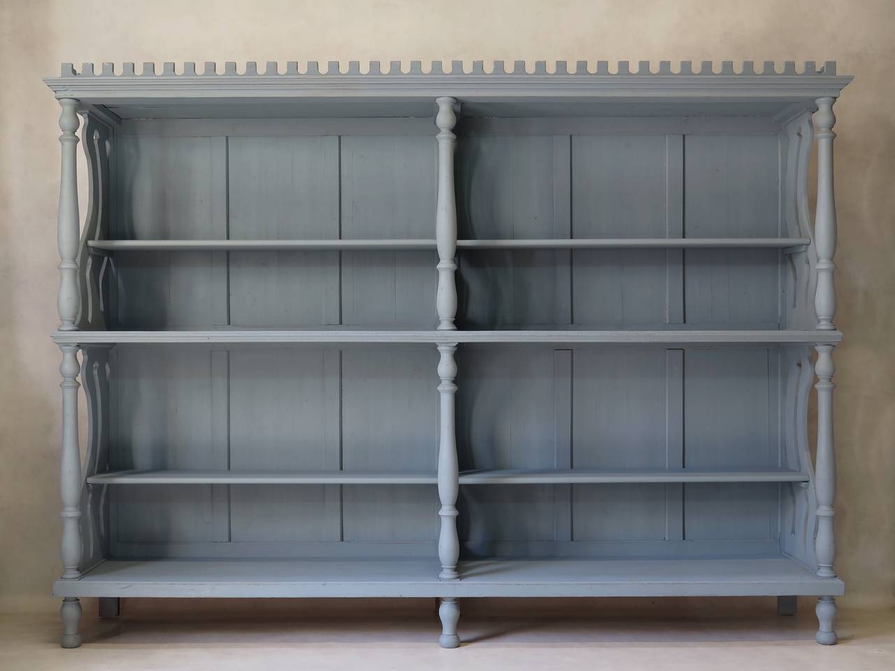 Elegant and unusual Art Nouveau bookcase, painted a soft blue/grey. Wavy cutout detail, columns and a crenellated cornice. 

Additional shelving can be easily added if necessary.