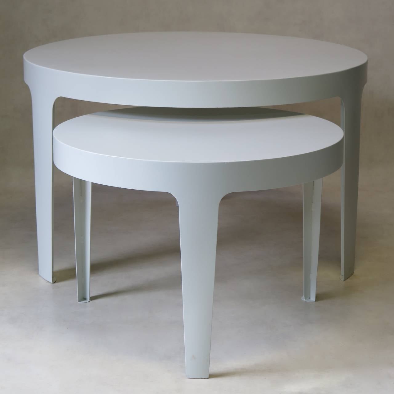 An alluring set of two chic and minimalist round metal tables, painted white. One is a dining table, the other a side/coffee table. Each table is made of one piece of iron, and has three simple, slightly tapering legs.

For indoor or outdoor