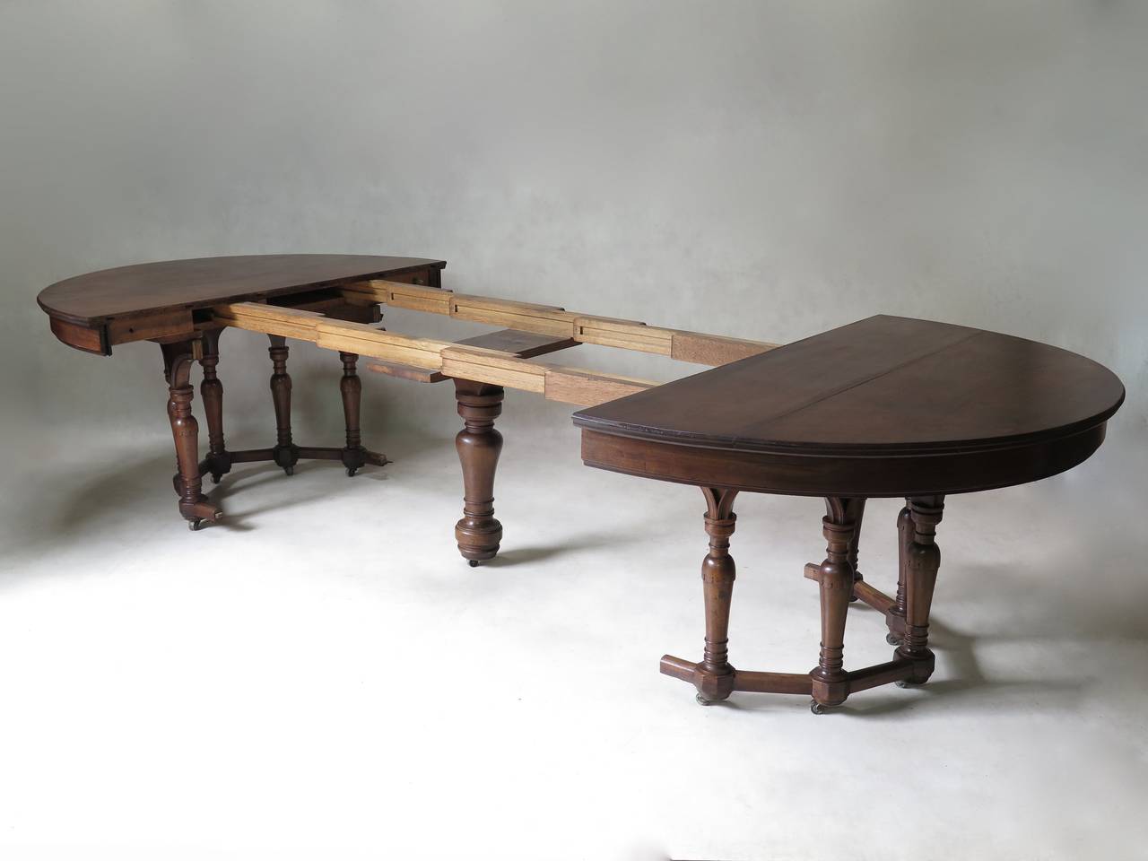 Rare and unusual oval dining table in solid walnut. Graceful turned and tapering carved legs, joined at the top by arches and at the bottom by a stretcher. Larger central baluster leg. The table is raised on casters.

The dining table comes with
