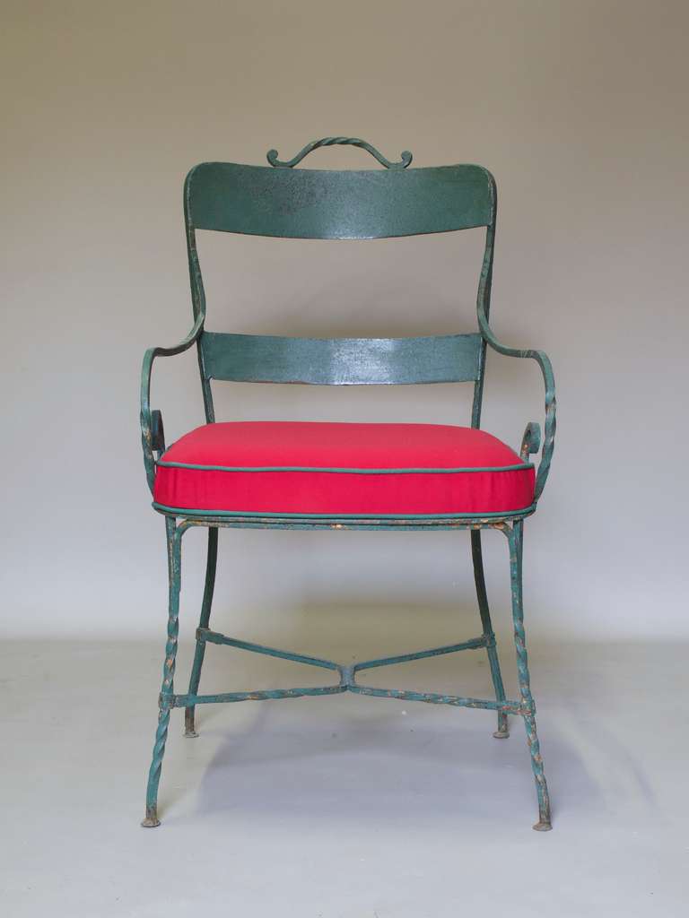 Lovely set of five wrought iron armchairs with faded green paint. Twisted iron detail on back handle, scrolled arms and front legs. X-shaped stretcher.

Very charming.

Seats upholstered in red canvas with green piping. For use indoors and out.