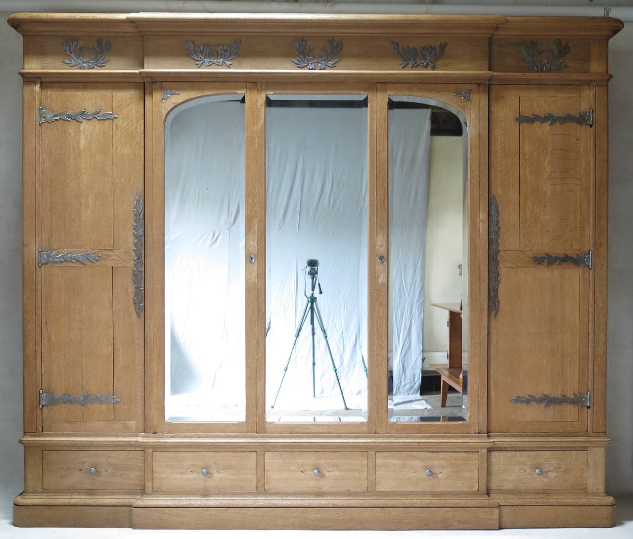 Impressive breakfront armoire in solid brushed oak, with four doors, and a central fixed door (see photo with doors open).
Unusual olive leaf motif hardware and appliquéd décor.
The three center doors are mirrored with original beveled