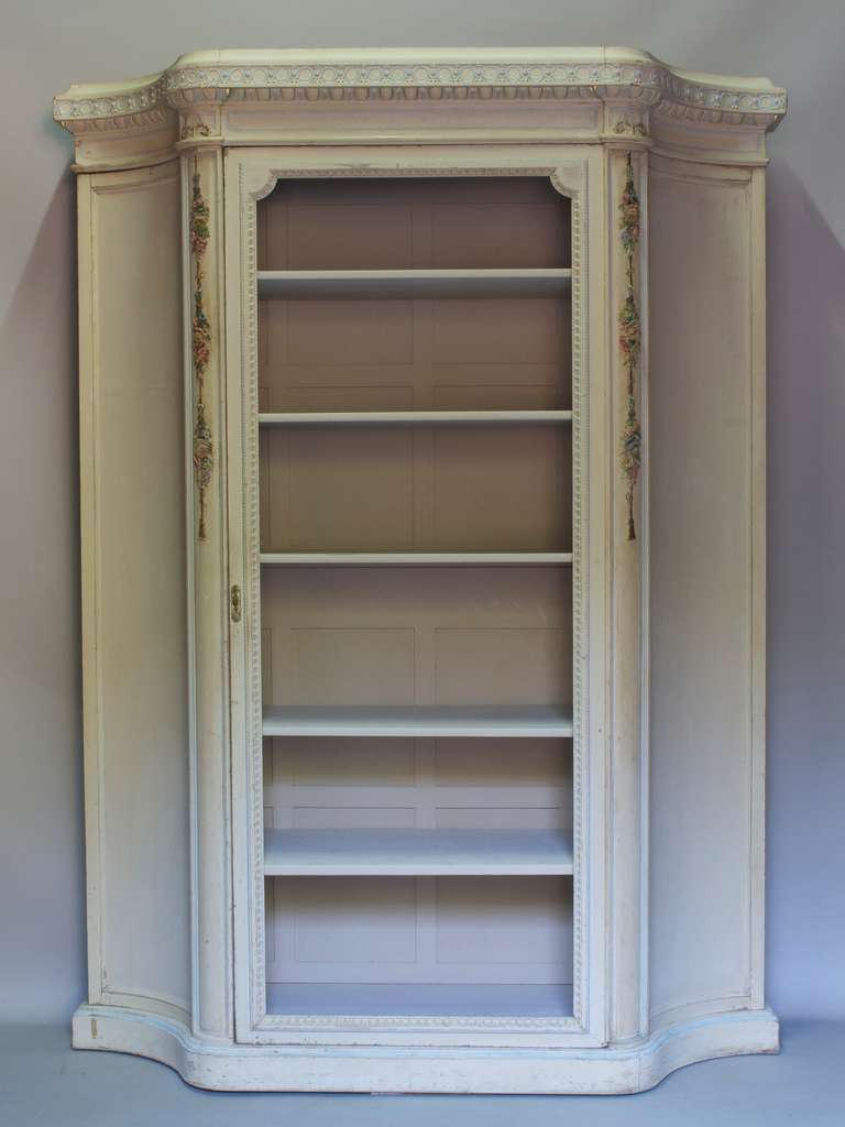 Insolito e grazioso armadio di grandi proporzioni, con lati concavi, interamente intagliato nel legno. Vernice color crema con dettagli in azzurro e oro. Il cornicione è decorato con un fregio con motivi di uova e dardi. Dettagli floreali intagliati
