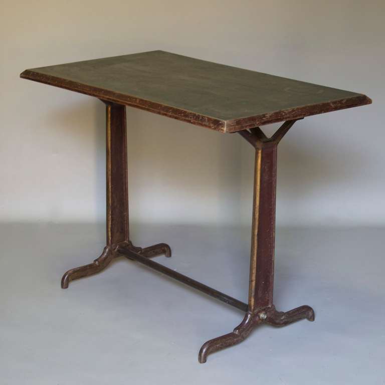 Charming rectangular café table with a heavy cast iron base (traces of gold paint visible), and a wooden top with a deep green textured finish.