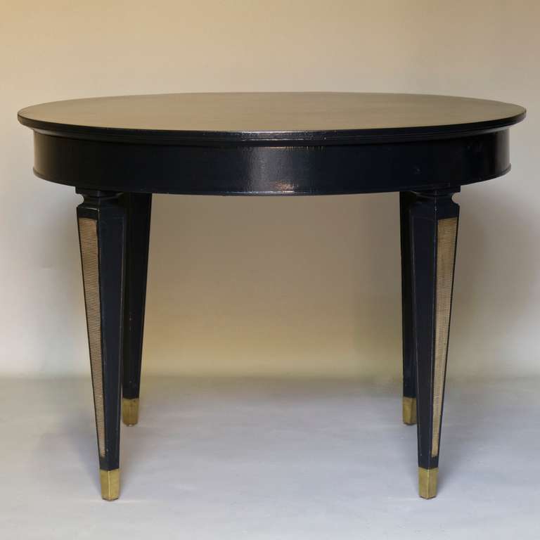 Circular dining or centre table by renowned French designer and decorator, Jean Pascaud.

The elegantly tapering legs are adorned with gilt bronze inlays and end in brass sabots. Glossy black finish.