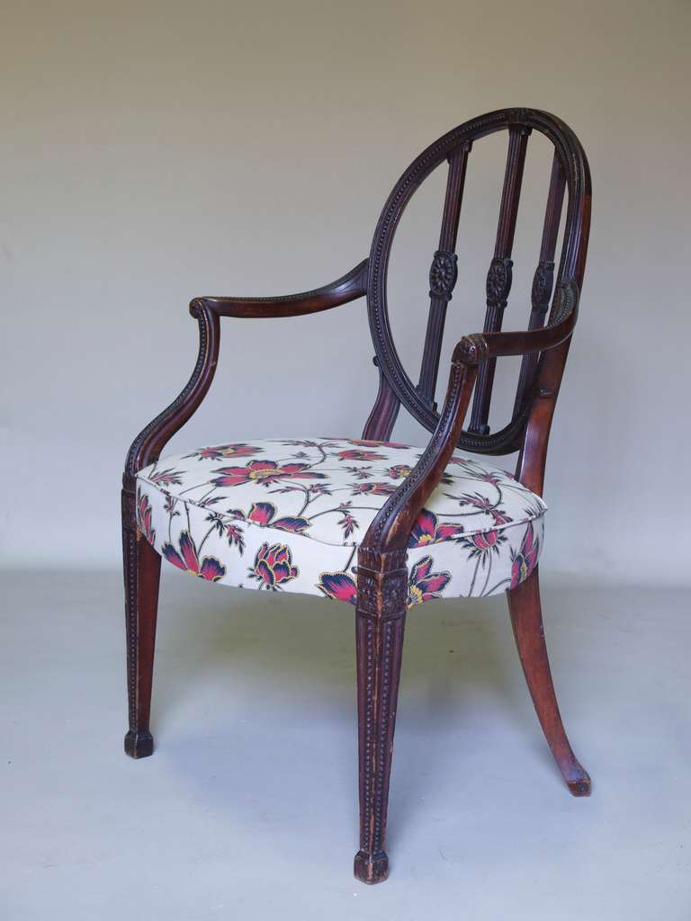 Wide armchair in the Hepplewhite style.

Shield back decorated with beading and rosettes.

Graceful movement: nice, outwardly curving arms, and serpentine seat.

Straight, tapering front legs with beading, ending in spade feet.