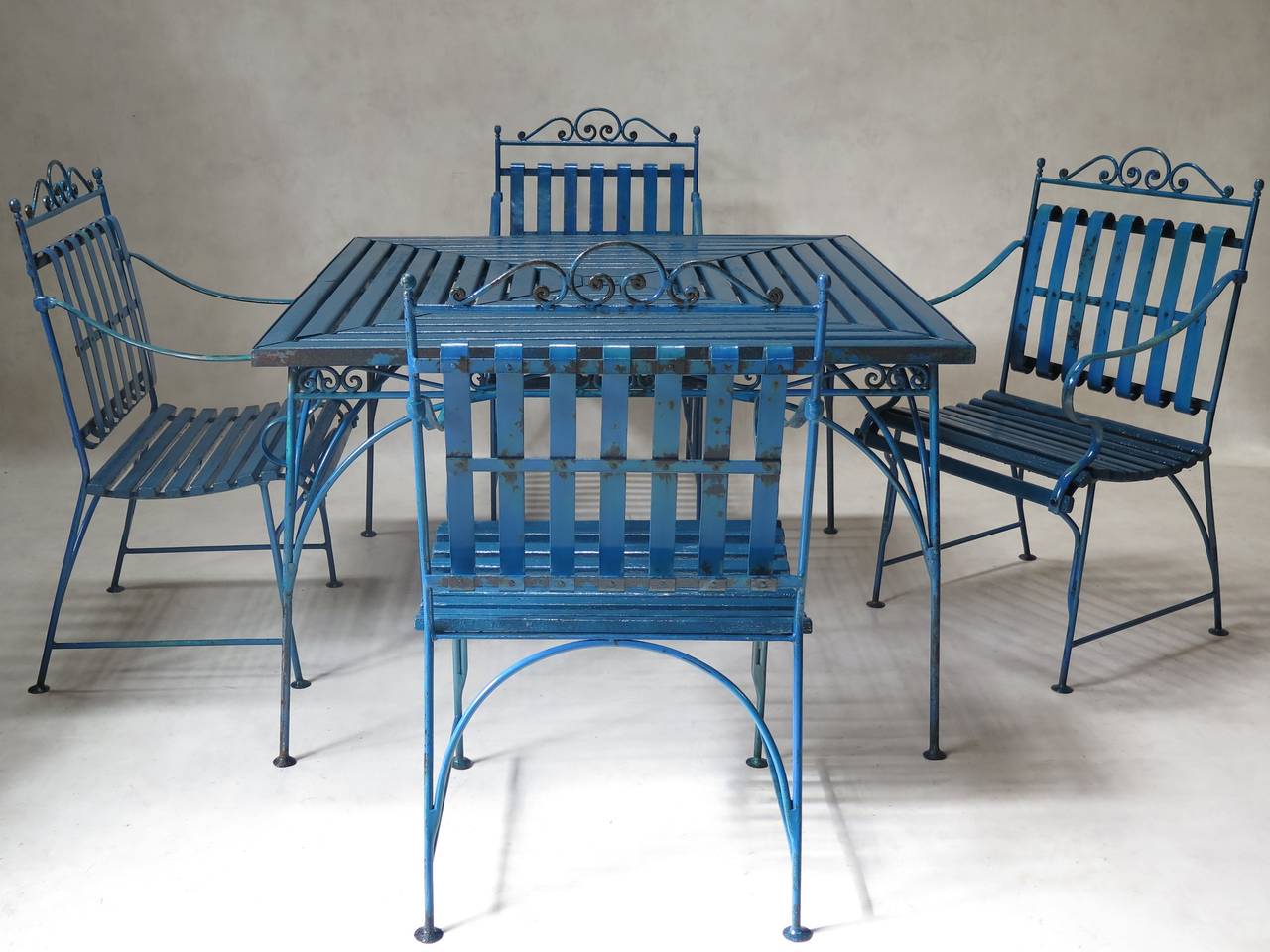 Elegant and unusual outdoor/garden dining set, comprised of a large square table and four large armchairs. The structure is made of hand-wrought iron, and the table top and chair seats are made of wooden slats.

There is a hole in the table centre