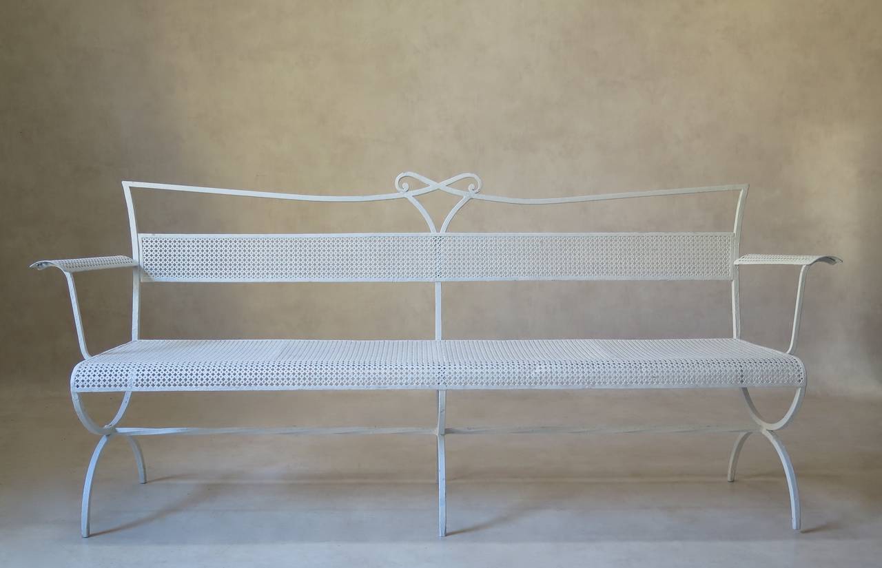 Elegant and chic long bench by Maison Jansen. Bow motif in centre of crest rail; curved armrests and seat edge. Raised on a Curule-shaped base, reinforced by a twisted iron stretcher. The back, seat and armrests are made out of cloverleaf patterned