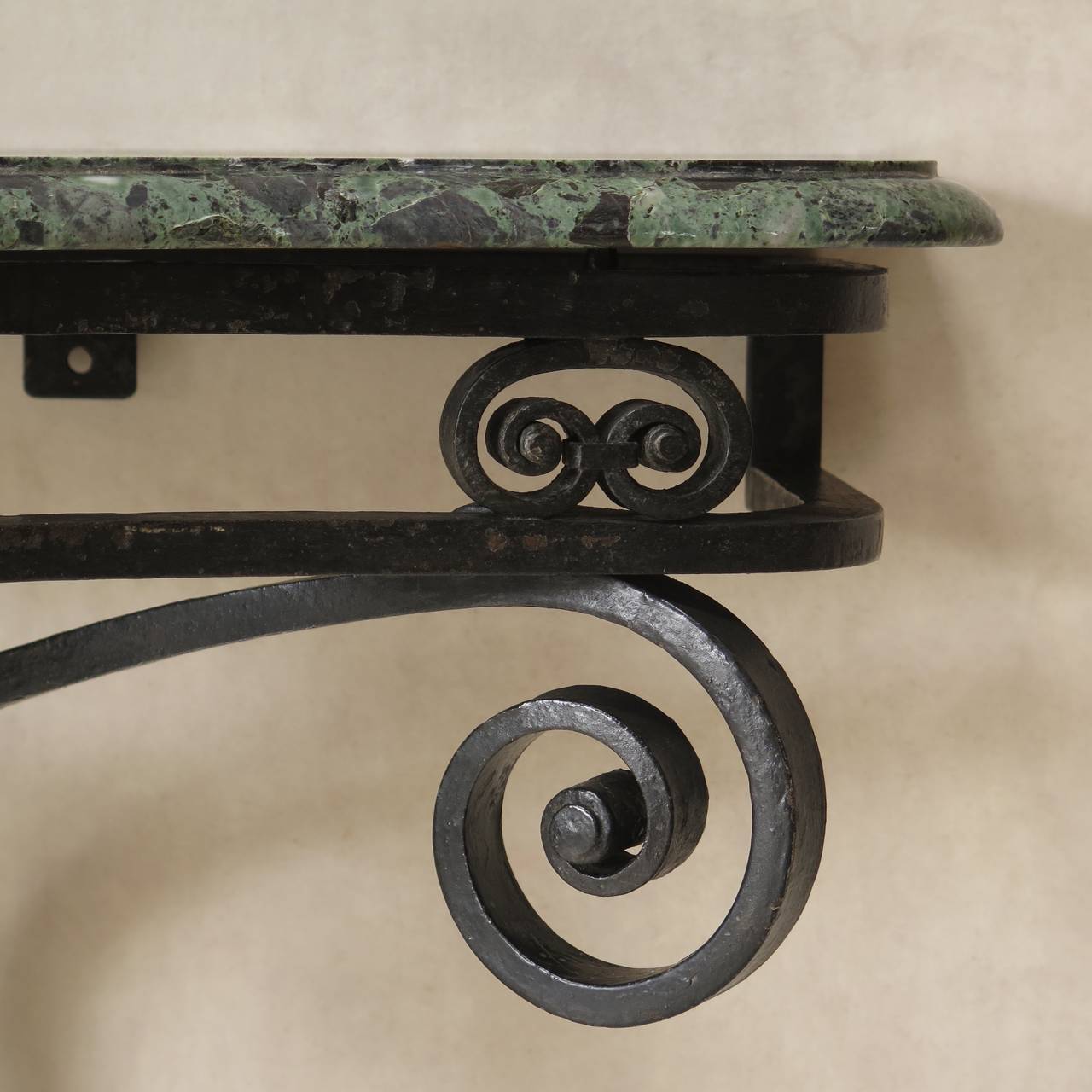 Chic pair of wall-mounted demilune consoles with scrolling wrought iron bases with original glossy black paint, and green marble tops.