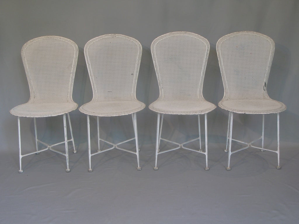 Set of four perforated iron chairs raised on elegant finely tapered legs, joined together by an X-shaped stretcher. 
Round seats with gently curving over around the edges. 
Original white paint and rubber feet.

