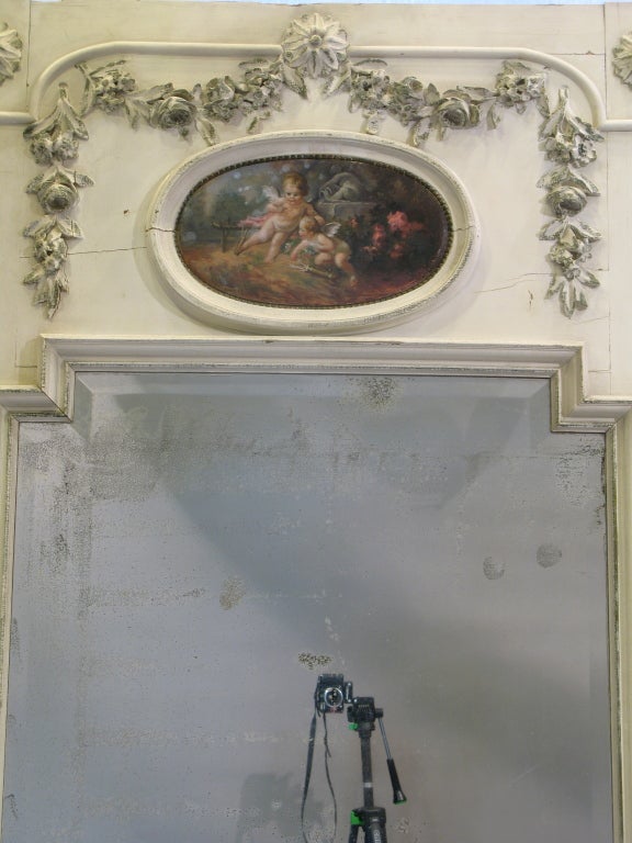 Large trumeau with original mercury glass mirror. The beveling follows the contours of the frame.

The top part is adorned with rosettes, a garland of wood-carved roses and foliage and a central oval medallion oil painting representing a pair of