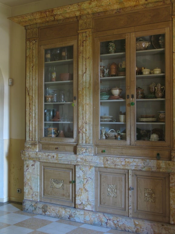 Pièce de mobilier très rare et étonnante. La structure (socle, colonnes et corniche) est peinte en trompe-l'œil de marbre. Les portes des armoires sont peintes en faux-bois. Des motifs floraux art déco sont sculptés sur les portes des armoires