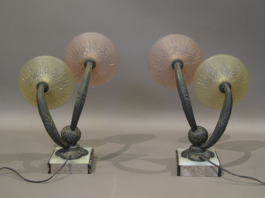 Handsome pair of French Art Deco period bronze and marble wall sconces in the style of Edgar Brandt. 

Bronze stems; black portor marble and onyx base; pink and yellow partly-frosted glass with geometric starlike design.

Very well-made.