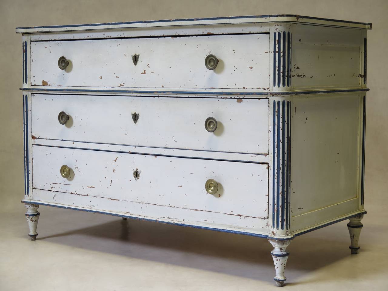 Charming Louis XVI three-drawer commode, flanked by fluted columns on either side, and raised on turned tapering feet. Round brass drawer pulls and shield-shaped keyholes. The commode was painted white a long time ago, with details elegantly picked