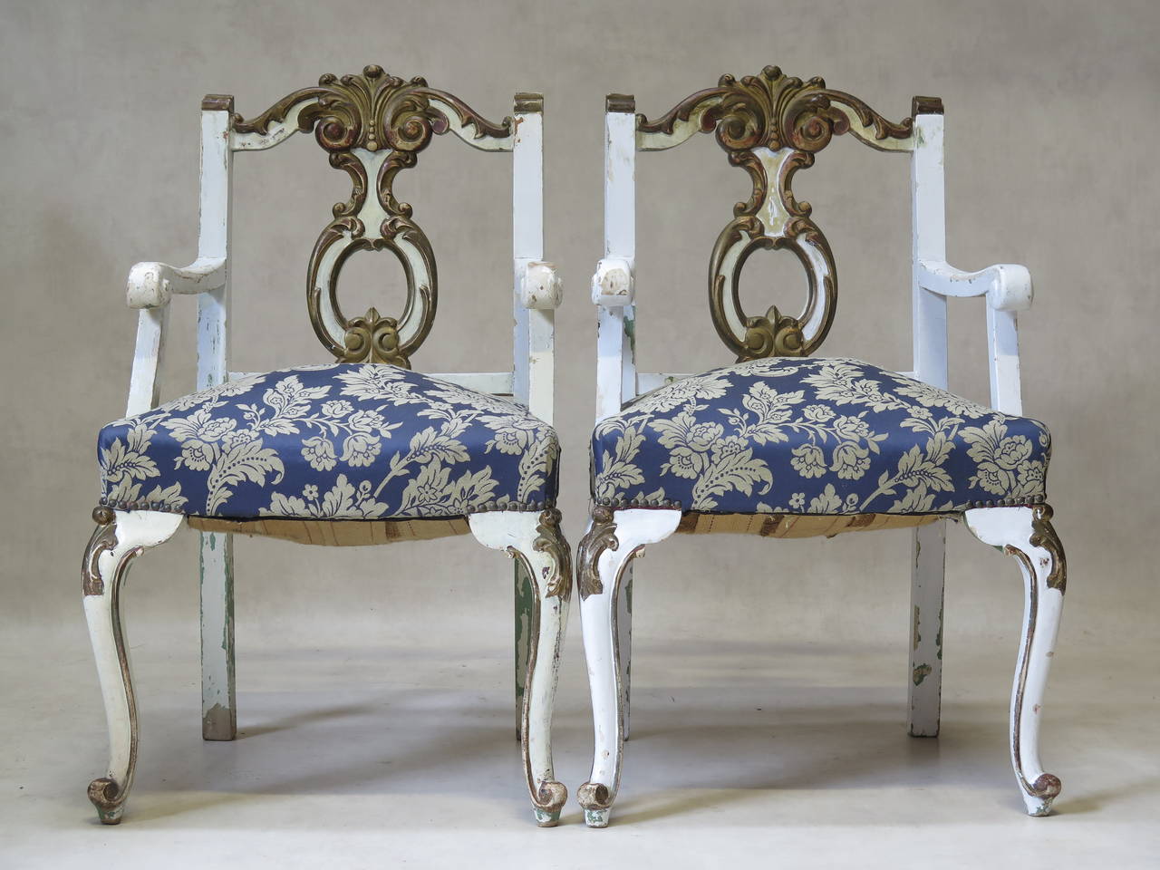 Charming pair of early twentieth century Louis XV style armchairs, painted white with burnished gold accents, and an earlier light green paint visible beneath. Boldly carved. The armrests end in scrolls. Cabriole front legs with embellished knees
