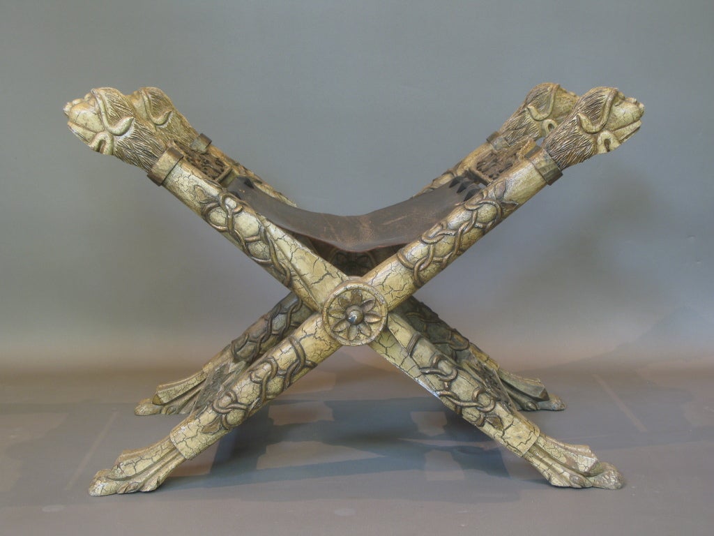 Aufwändig geschnitzter Klapphocker, mit Löwenköpfen an den oberen Enden und Löwentatzen am Sockel. Craquelé-Farbeffekt.

Sitz aus Leder.