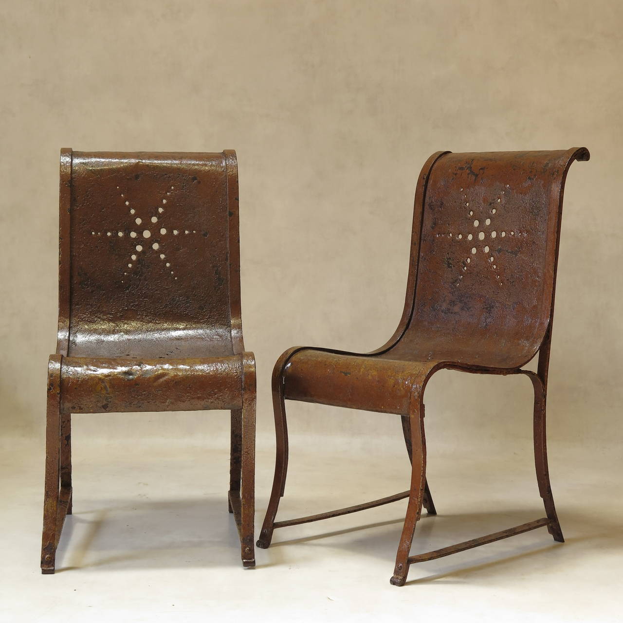 Charming and uncommon set of four riveted wrought-iron chairs of unusual design, with cutout star patterns in the backs and seats. Original brown paint, which has acquired a lovely patina over time.
Originally designed as garden furniture, these