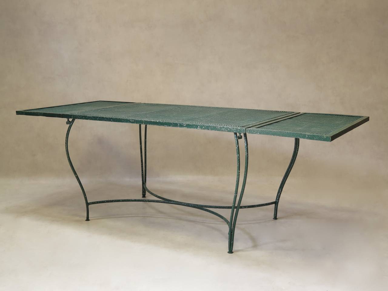Charming wrought iron dining table, with extensions (fixed) on either end of the central table top, made out of cloverleaf-patterned sheet metal, with a two-centimeter wide frame around the contours. Raised on double tapering cabriole legs, joined