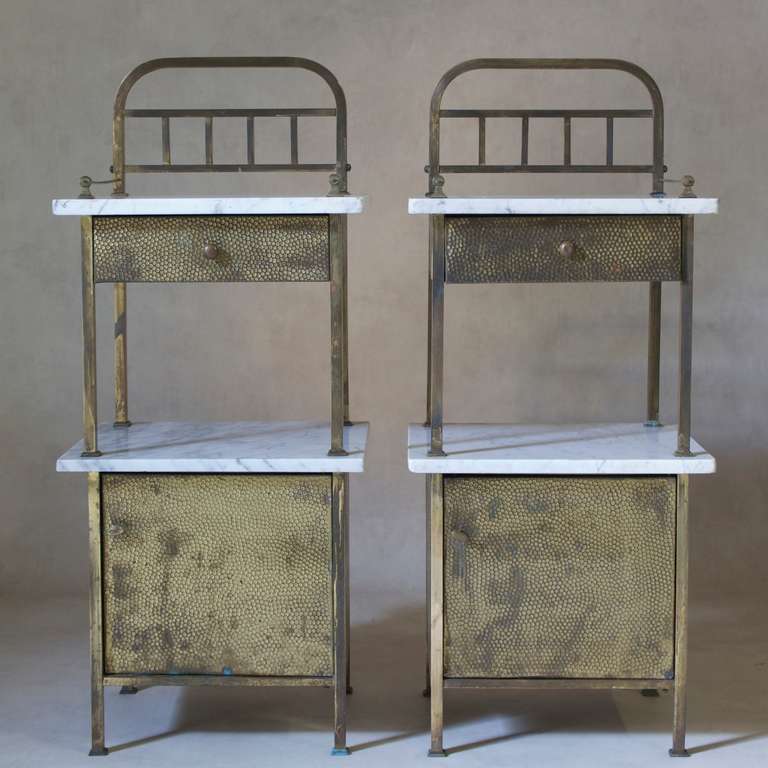 Chic matching pair of French night stands dating from the 1940s.

Each table has two marble-topped tiers (white with light grey streaks), a lwoer cupboard compartment, and a drawer.

Gilt and hammered-iron finish.