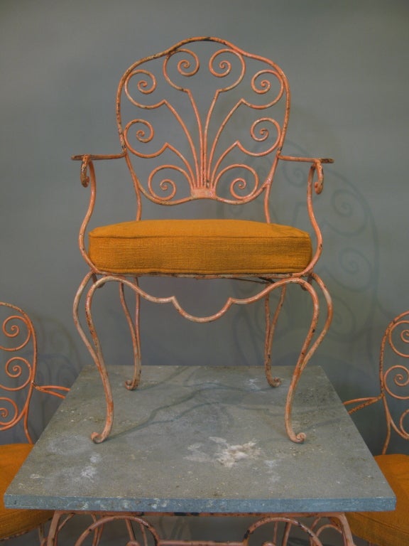 An elegant set comprising four armchairs and a table of wrought iron with original orange paint.

The table has its original square stone top, and has acquired a nice patina.

The armchairs are of Louis XV inspiration, with a lovely fan-shaped