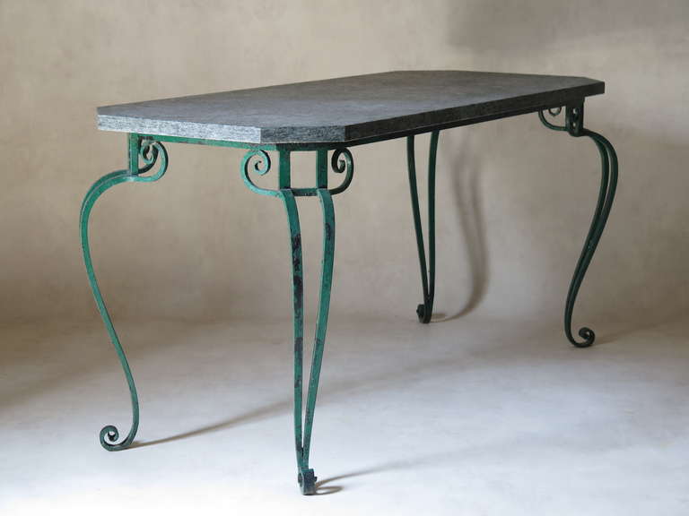 Wrought-iron set of two chairs and a rectangular table with lovely scrolled feet and ironwork, in original green paint.

The chair seats are upholstered in blue outdoor fabric. 

The table top is of grey marble, and has canted corners.

The