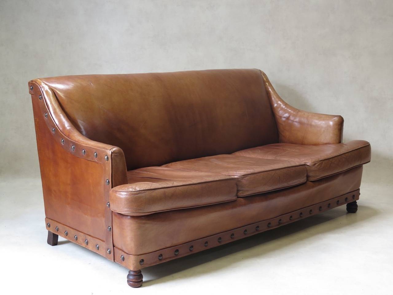 Comfortable and large living-room set comprised of two club chairs and a three-seat sofa (pull-out), upholstered in thick cognac-colored leather with large brass nail trim.

Dimensions provided below are for the settee. The armchairs measure (in
